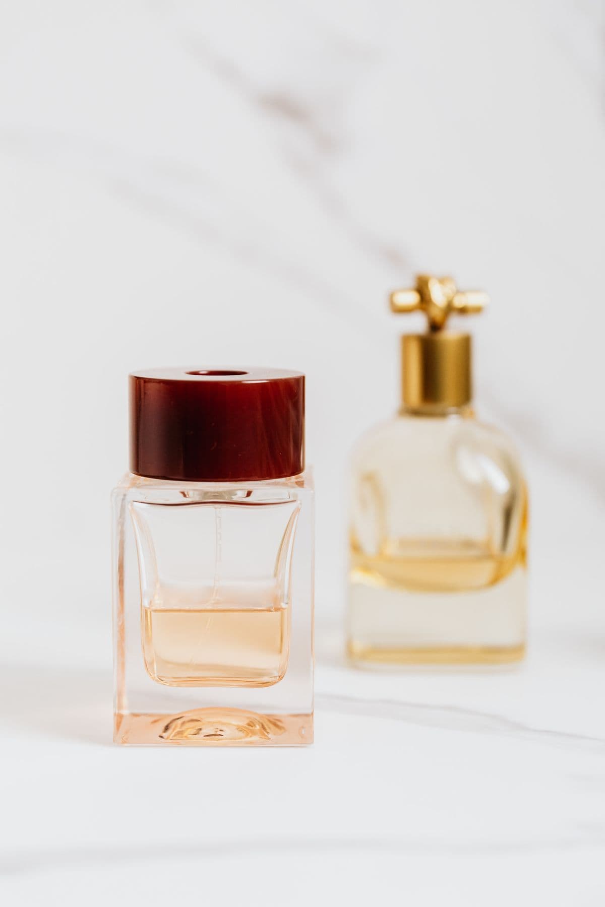 A blush-toned flacon paired with a golden bottle on marble